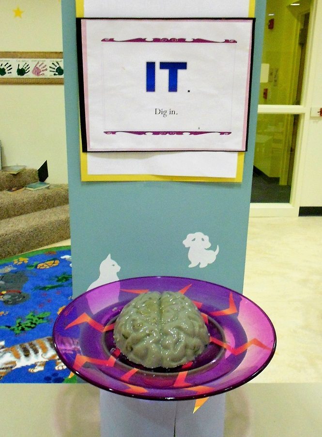 Brain-shaped gray gelatin on a purple plate with lightning bolts, with a sign reading "IT: Dig in."