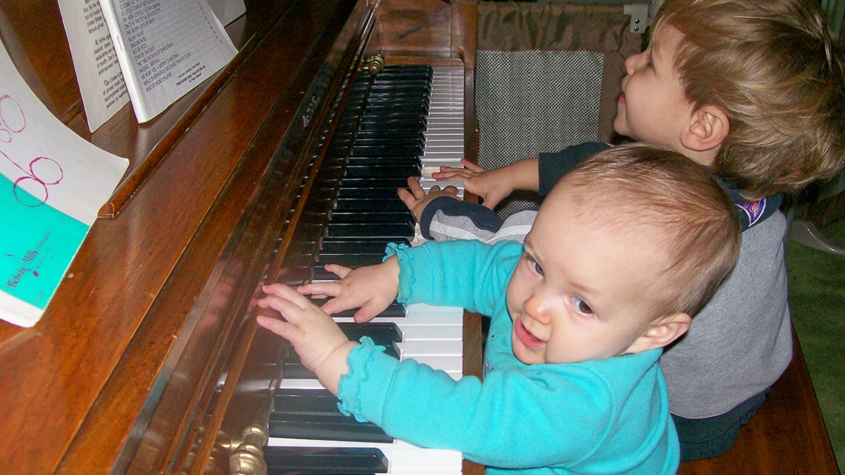 Two toddlers sitting at an upright piano, appearing to sing and play