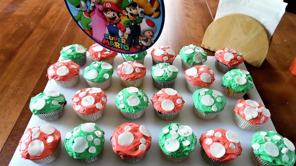 Tray of cupcakes, decorated like Super Mario powerup mushrooms, with white fondant polka dots on red or green icing.