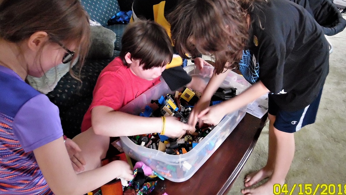 Children bending over a large bin of Lego on a coffee table, sorting through looking for pennies.