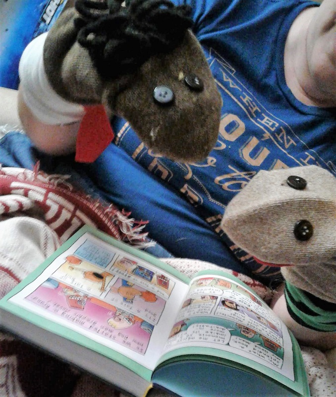 George and Harold sock puppets (on the hands of this writer) looking over one of the first pages of 'Dog Man and Cat Kid'