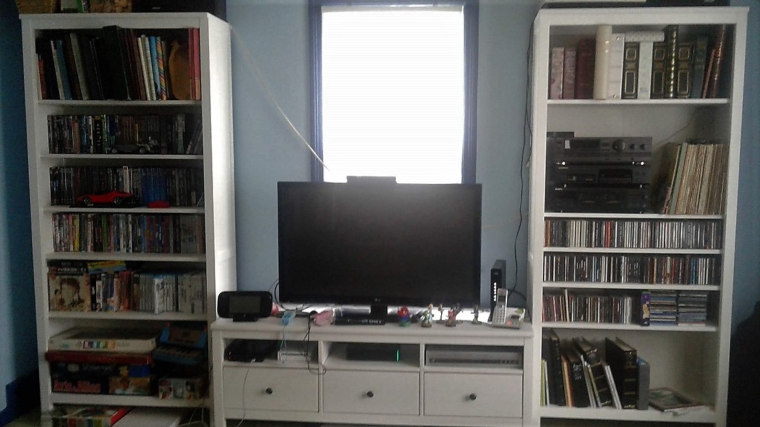 two tall bookcases flanking a white TV stand, all shelves full of albums, CDs, and DVDs