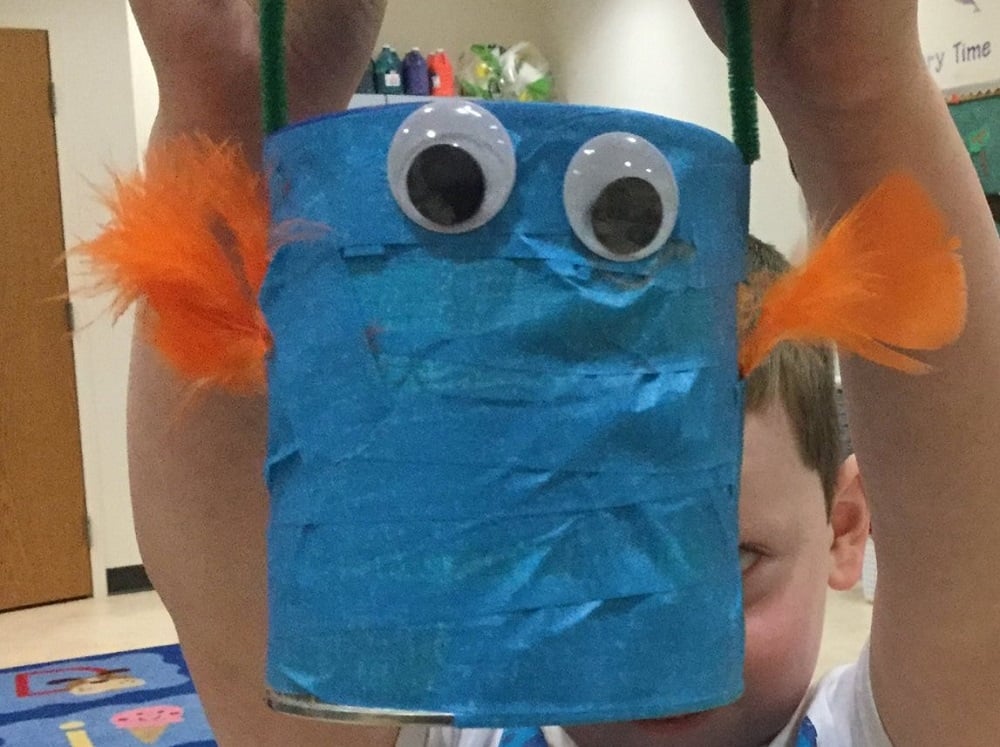 cylinder covered in blue masking tape, with two orange feathers sprouting out of the sides and two big googly eyes