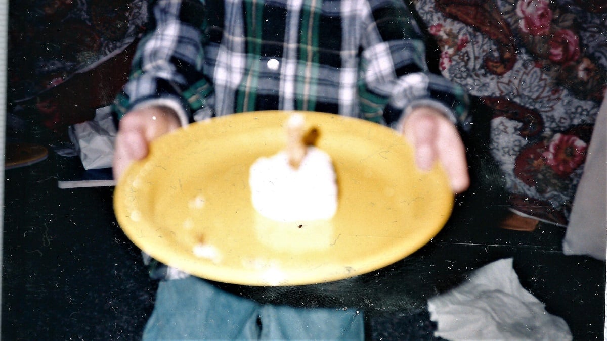 Child holds a plate to the camera that contains a blurry snack cake with pretzels sticking out of the top