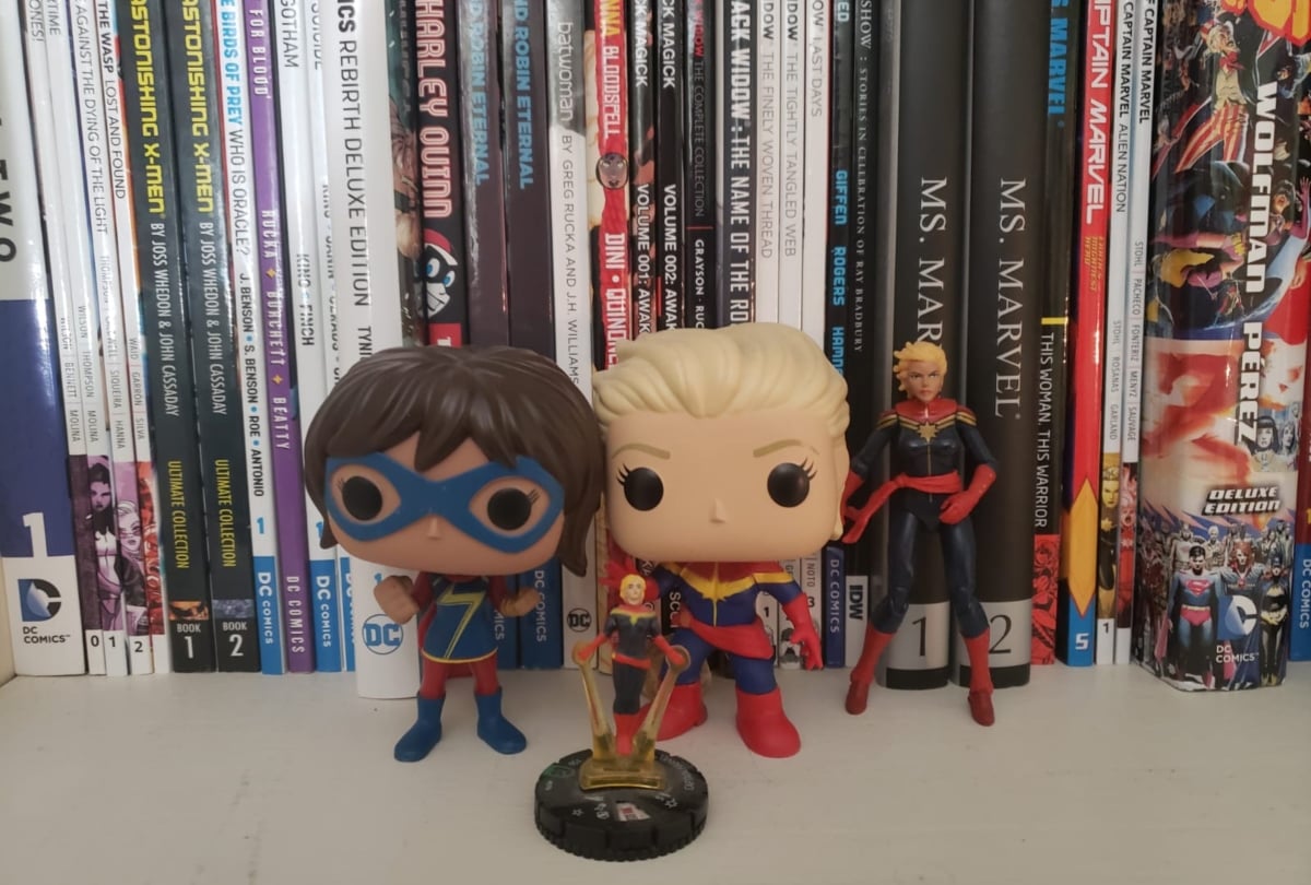 Figures of Kamala Khan and Carol Danvers as Captain Marvel set against a shelf of comic books.