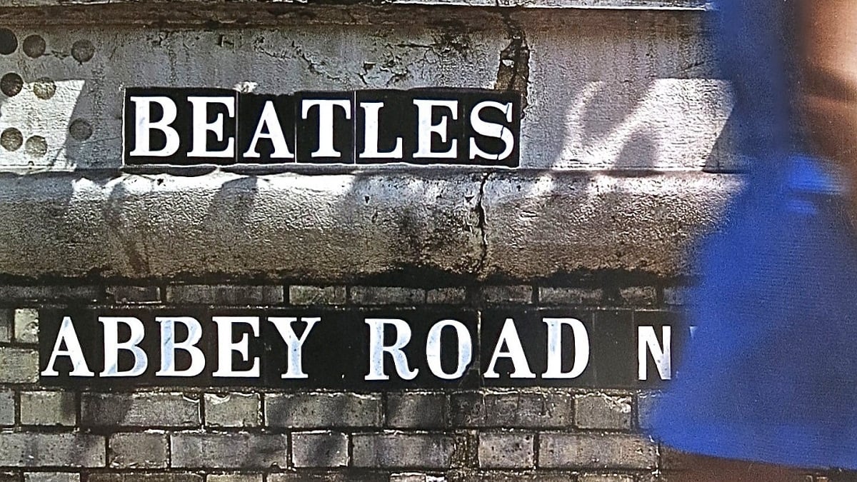 widescreen crop of the back cover of the Beatles' 'Abbey Road' album which shows the letters of artist and title embedded in a stone wall as a woman walks past
