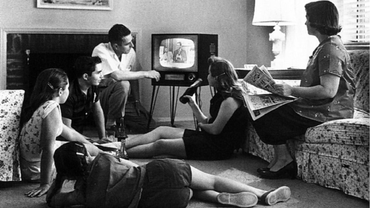 B/w photo of a Caucasian family made up of a man, woman, two teenagers and a preteen, watching television circa 1958