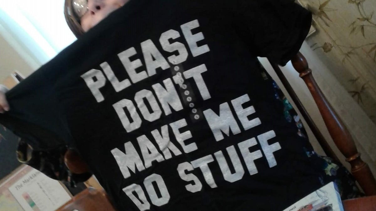 Barely visible pre-teen holds T-shirt that reads "PLEASE DON'T MAKE ME DO STUFF"